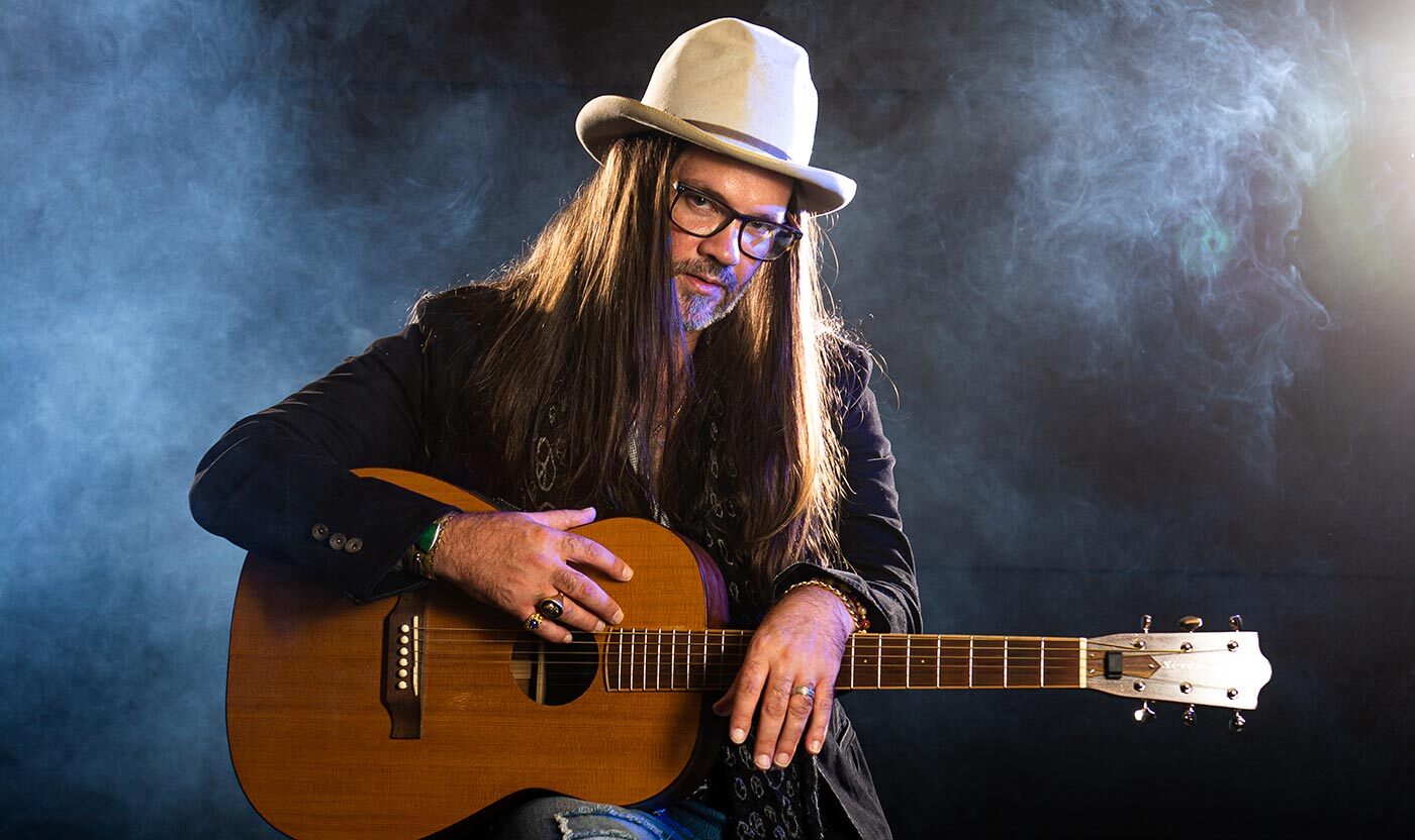 Bo Bice holding an acoustic guitar against a smoky studio backdrop